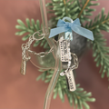 Decorative glass ornament with charms and a blue ribbon on a branch.